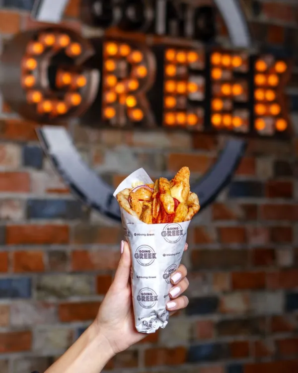 Hand holding loaded fries with Going Greek sign in background